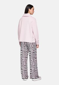 Light pink oversized sweatshirt with a folded collar, paired with wide black and white checkered pants featuring a wavy pattern. White sneakers.