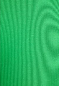 Grön tyg med tät vertikal ribbad stickningstextur, jämnt fördelad och konsekvent i mönster och färg.
