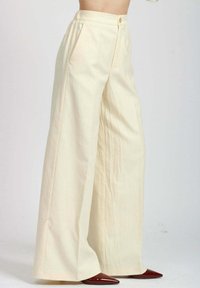 Pantaloni ampi color crema con finitura testurizzata, dotati di tasche frontali e chiusura con un solo bottone. Abbinati a decolletè rosse a punta.