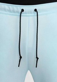 Pantalones cortos deportivos de color azul claro con cintura elástica, con cordón negro y puntas de plástico, textura suave y diseño simple.