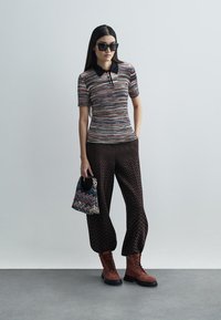 Kootud polo särk mitmevärvilise mustriga ja musta kraega, koos pruunide zigzag-mustriga pükste ja pruunide pitsidega saapatega.