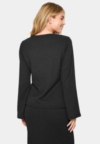 Top nero a maniche lunghe realizzato in un tessuto testurizzato e con scollatura quadrata. Il retro presenta cuciture verticali e una vestibilità comoda.