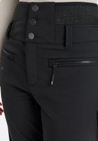 Zwarte broek met een hoge tailleband en drie metalen knopen. Bevat twee met rits gesloten zakken en een soepele, gestructureerde stof.