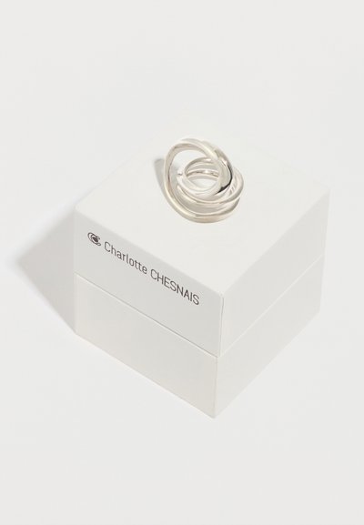 Ασημένιο δαχτυλίδι με στριφτή λεπτομέρεια πάνω σε λευκό κουτί με μαύρα γράμματα, με λείο φινίρισμα και διασυνδεδεμένο κυκλικό σχέδιο. Το κουτί φέρει την ένδειξη "Charlotte CHESNAIS."