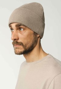 Gebreide beanie in lichtbeige met een geribde textuur. Het ontwerp is aansluitend en heeft een subtiele naaddetail op de kroon.