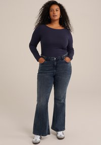 Top de manga larga azul marino combinado con jeans de mezclilla oscuros de talle alto y acampanados. Los jeans tienen bolsillos frontales y un cierre de botón. Zapatillas deportivas blancas.