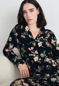 Zwart pyjama set met bloemenpatroon in zachte stof, bestaande uit een knoopshirt met een zak en lange mouwen, aangevuld met bijpassende broek.