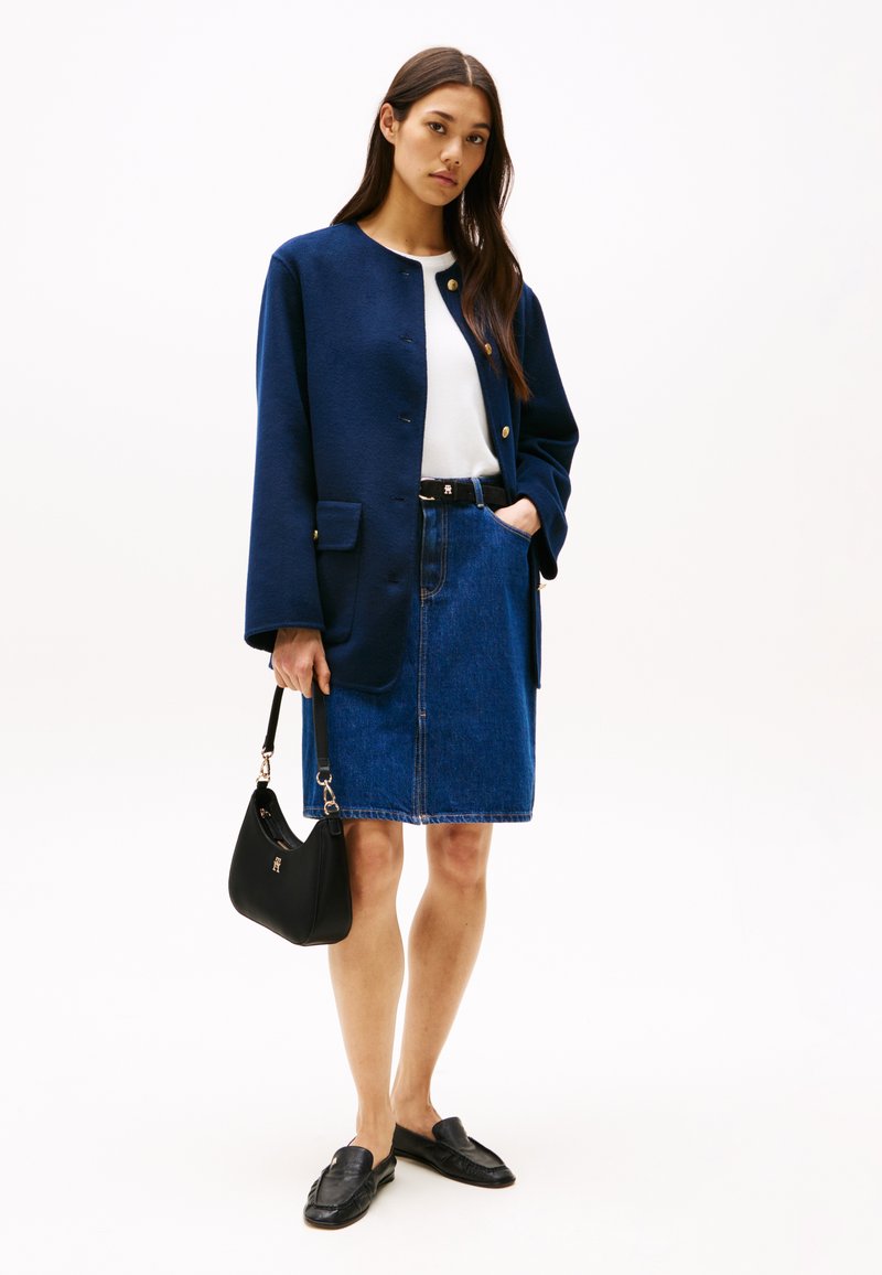 Navyblauwe wolmixjas, witte overhemd, denimrok, zwarte riem, zwarte handtas en zwarte instappers. Bevat gouden knopen en zakken.