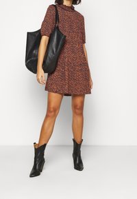 Blommönstrad klänning med korta ärmar, i orange och svarta nyanser. Matchad med en svart läderhandske och svarta ankelstövlar.