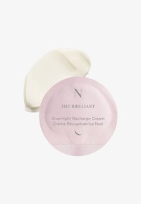 Crème de recharge nocturne dans un emballage rond et rose avec du texte argenté. Un échantillon de produit crémeux, de couleur blanc cassé, montre une texture lisse.