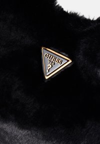Sort fløjl med et blankt sort trekantet logo, der har "GUESS USA" i guld og et spørgsmålstegn som accent. Blød tekstur, elegant design.