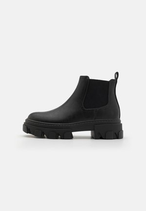 Schwarze Chelsea-Stiefel mit einem glatten Leder-Obermaterial, elastischen Seitenteilen und einer klobigen Gummisohle mit einem Zickzackprofil.