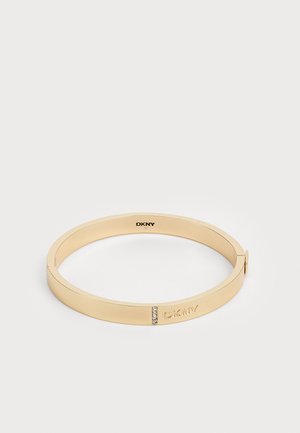 Zlato obarvana kovinska bangle zapestnica z gladko površino, ki ima majhen vrstico kristalov in vgraviran DKNY logotip na eni strani.