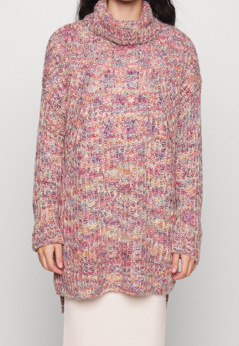 Femme portant un pull à col roulé tricoté épais multicolore avec des manches longues et un motif côtelé.
