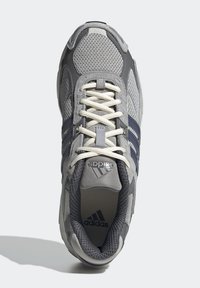 Šedá sportovní bota s vrchním dílem ze síťoviny, třemi tmavě modrými pruhy, krémovými tkaničkami a strukturovanou gumovou podrážkou, značená logem adidas.