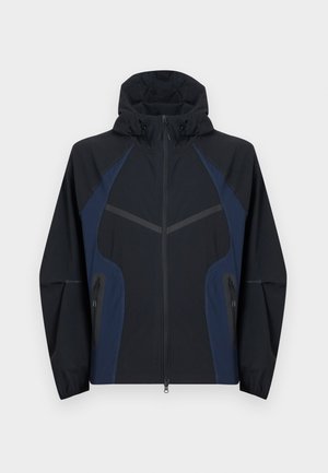 Veste à capuche noire et bleu marine avec fermeture éclair complète à l'avant, deux poches latérales zippées et poignets élastiques aux manches longues.