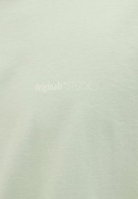 Light green T-shirt with a soft texture features embroidered logo "Originals STUDIO" in a slightly lighter shade.