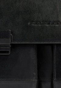 Zwarte leren documentenmap met een gladde textuur, gestructureerde vorm, geperst logo en een metalen sluiting.