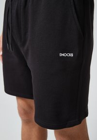 Zwarte katoenen shorts met een elastische tailleband en koord. Bevat zijzakken en een wit geborduurd "SNOCKS" logo op de dij.