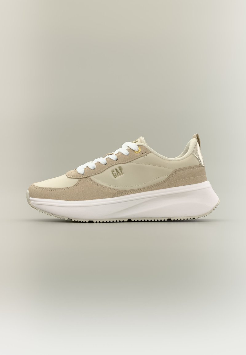 Μπεζ και κρεμ αθλητικό παπούτσι με λευκά κορδόνια και παχύ λευκό πέλμα, με τη σήμανση «GAP» στο πλάι, παρουσιάζεται σε καθαρή πλευρική όψη.