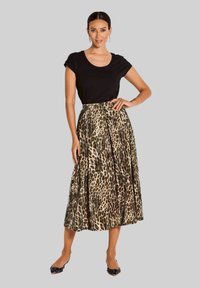 Vrouw die met haar hand op haar heup staat, gekleed in een zwarte korte mouwen top, een midi-rok met luipaardprint, en puntige flats met versieringen.