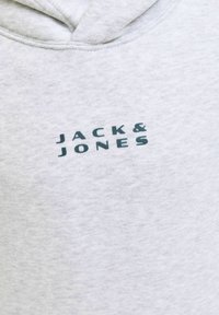Sudadera gris hecha de una tela suave con un bolsillo canguro. Presenta un logo frontal "JACK & JONES" en impresión verde oscuro. Diseño tipo pullover con capucha.
