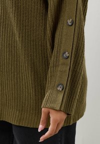 Olive green sweter dzianinowy z teksturowanym wzorem, z prążkowanym dołem i trzema ciemnymi guzikami przy rękawie dla dodatkowego akcentu.
