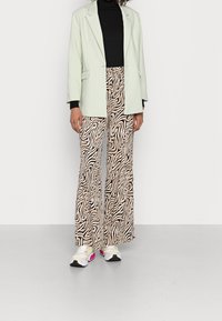 Mintgrön oversized blazer, svart rullkrage, och krämfärgade utsvängda byxor med ett svart och beige vågmönster, ihop med vita sneakers.