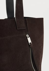 Καφέ τσάντα ώμου από σουέτ με δομημένο σχήμα, που διαθέτει ασημί φερμουάρ και μαύρες δερμάτινες λαβές. Ιδανική για καθημερινή χρήση.