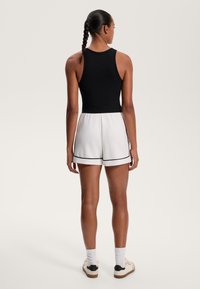 Fekete bordás ujjatlan felső, amit fehér, fekete szegélyű sorttal párosítottak. A modell egy fonott copffal áll, bemutatva a hátulról készült nézetet.