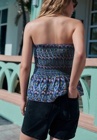 Axelbandslös, rynkad peplumtopp i blått tyg med flerfärgat blommönster; kombinerad med svarta jeansshorts med sidfickor.