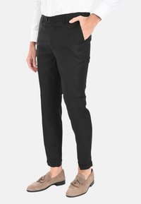 Pantaloni neri su misura con una vestibilità slim, passanti per cintura, tasche laterali e una texture liscia. Abbinati a mocassini beige.