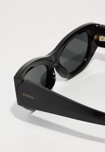 Óculos de sol pretos com acabamento brilhante, design angular e lentes verdes. Apresenta o logótipo 'Burberry' em dourado na haste.