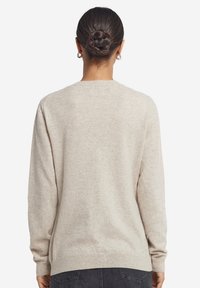 Beige stickad tröja med rundad hals, långa ärmar och ribbade muddarna och fållen. Mjuk textur, enkel design, inga mönster eller utsmyckningar.