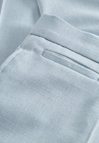 Lichtblauwe stoffen broek met een gestructureerde weving, voorzien van een net afgewerkte achterzak en strakke lijnen door het hele kledingstuk.