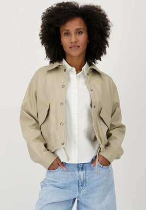 Beige cropped jack gemaakt van glad materiaal, met drukknoopjes, een overhemdkraag en een verstelbare drawstring aan de zoom. Gecombineerd met een wit shirt.