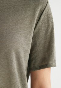 Oliven grøn t-shirt stof med en blød tekstur, med en klassisk rund hals og korte ærmer. Søm detaljer er synlige.