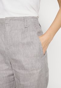 Ljusgrå linbyxor med en avsmalnande design, som har sidofickor och en subtil textur. Midjebandet har sömdekoration.