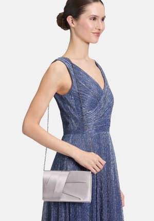 Zilveren satijnen clutch met decoratieve plooien en een kettingband, vastgehouden door een persoon in een blauwe jurk met een textuurpatroon.
