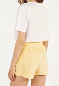 Vit kortärmad skjorta och gula badshorts i frotté med elastisk midja, med en slät textur och avslappnad passform.