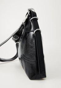 Borsa a spalla in vernice nera con tracolla regolabile e anelli in metallo argentato, vista di lato su uno sfondo bianco.