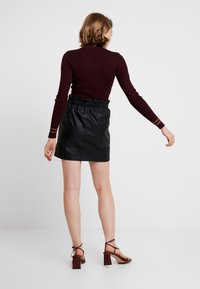 Minifalda de cuero negra con una cintura elástica, combinada con un suéter de canalé burdeos ajustado que presenta rayas en contraste en las mangas.