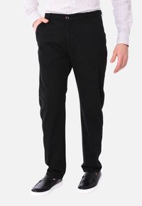 Pantaloni neri dal fit rilassato, con chiusura a bottone e tasche laterali, abbinati a eleganti scarpe slip-on nere.