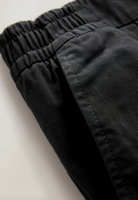 Black fabric pants with an elastic waistband, featuring a smooth texture and clean seams. The image shows a close-up of the waistband and fabric.