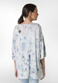 Kevyt, löysä blouse pehmeästä materiaalista, jossa on sininen kukkavesiväri kuvio, kolmannelta neljännekseltä hihnat ja pyöreä pääntie.