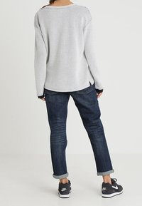 Suéter gris texturizado con un escote redondeado, combinado con jeans de puño enrollado de color azul oscuro y zapatillas deportivas negras.