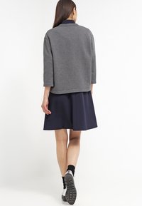 Harmaa, ylisuuri takki, jossa on kolme neljännesosahihastoa, päällä tummansininen hame. Sileä pinta, kaulustyyli ja rento muotoilu.