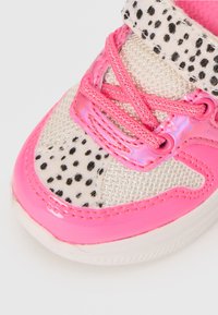 Rosa sportskor med överdel i mesh och svarta prickiga accenter, glänsande lackdetaljer och kontrasterande rosa snörning.