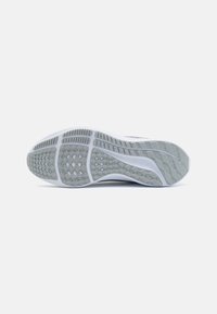 Suela de una zapatilla de running blanca y gris con patrones de agarre texturizados y un logotipo de Nike visible sobre un fondo blanco.