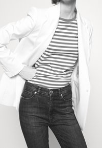 Blazer blanco superpuesto sobre una camiseta de rayas gris y blanca, combinado con jeans de mezclilla oscura. Enfoque en texturas y contrastes de color.